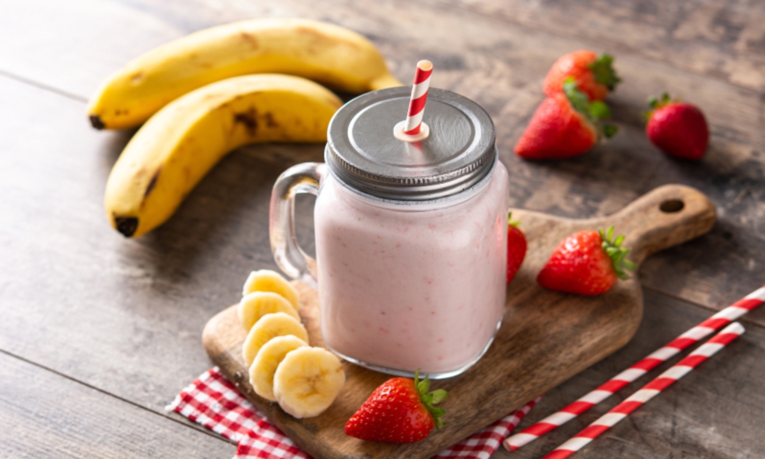 Owocowe smoothie w kubku, obok znajdują się składniki na smoothie: banany i truskawki.